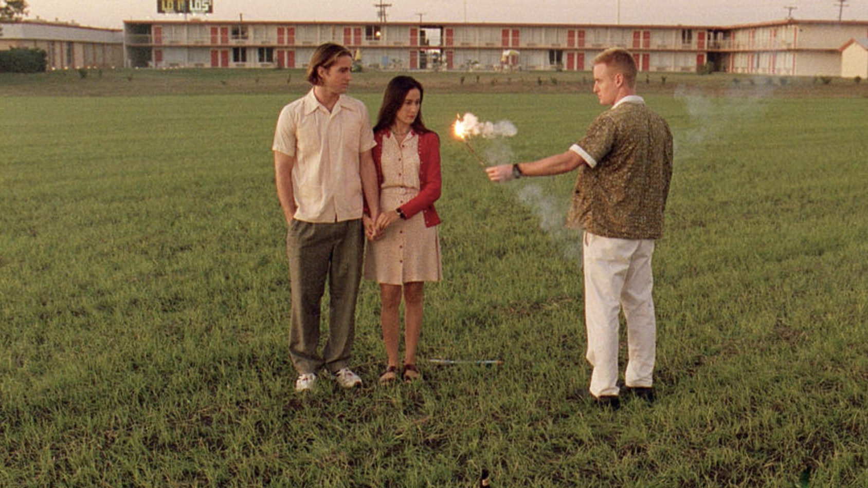 A still from the movie Bottle Rocket in which main characters Dignan, Anthony and Inez stand on a lawn next to a motel.